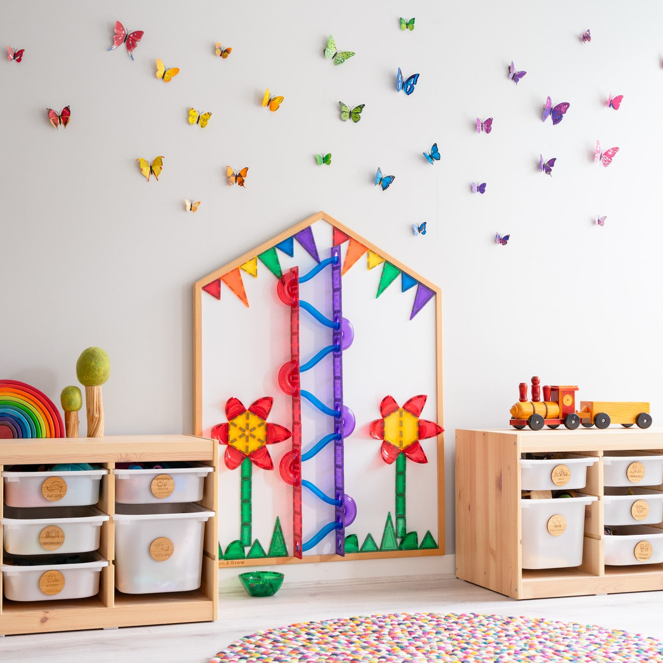 Multi-Board set up on wall with rainbow coloured ball run and poppies made of magnetic tiles with colourful butterflies on wall in a playroom