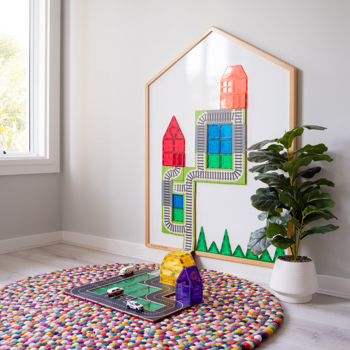 Learn & Grow Toys Multi-Board with whiteboard stuck to wall with train and road toppers on the board with colourful rug on floor