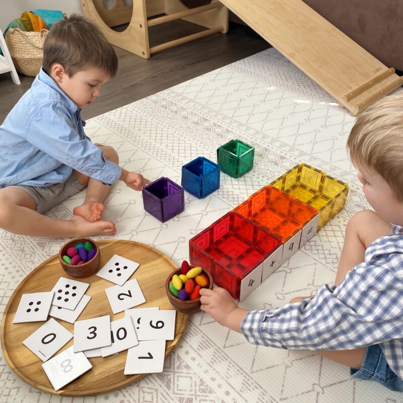 2 children playing with wooden grapat mandalas and numeracy tile toppers with wooden play equipment in background