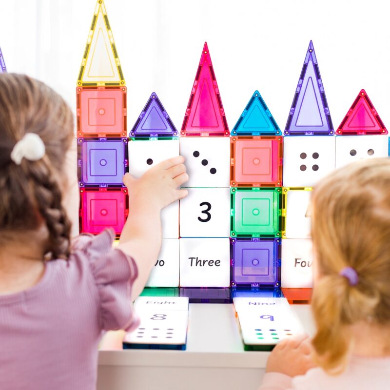 2 girls playing with numeracy toppers set up on a magnetic tile castle