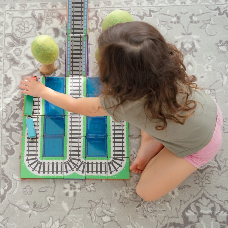 Child playing with magnetic tile train toppers with magnetic tiles and wooden trees