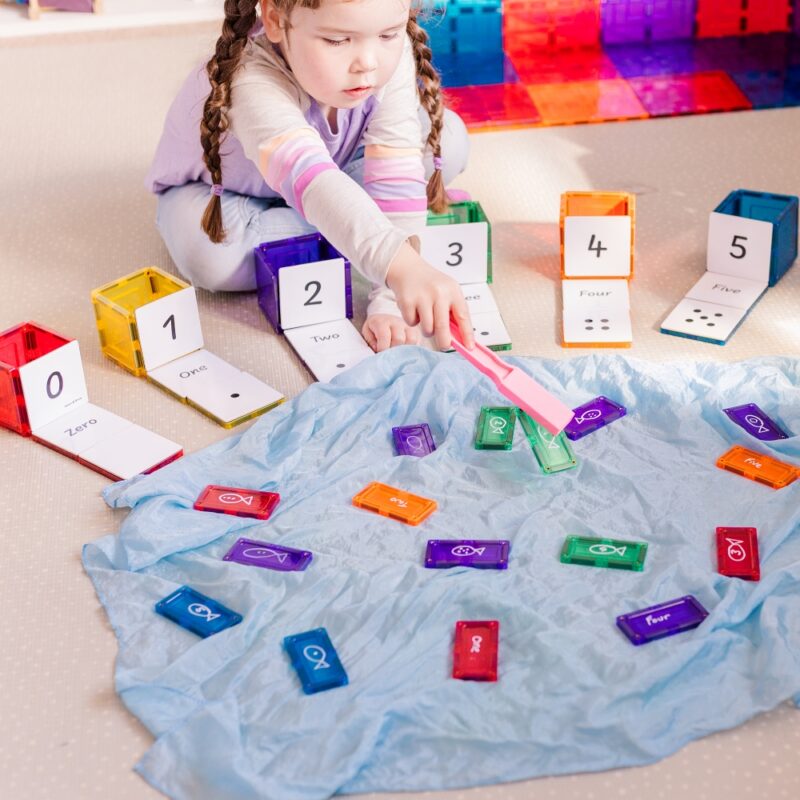 Child playing with magnetic wand and numeracy toppers and magnetic tiles on blue playsilk