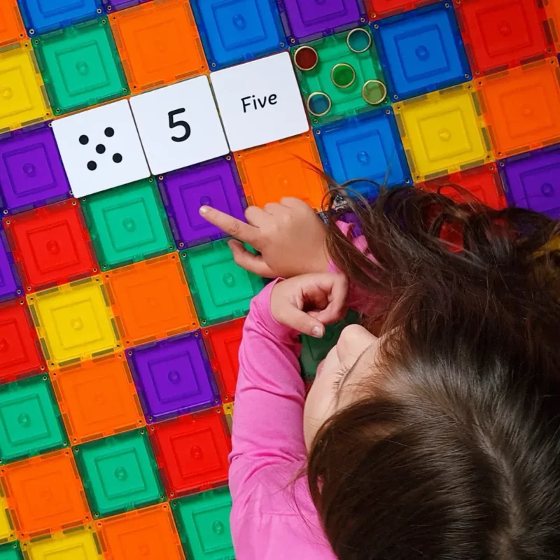 Child pointing to number 5 on rainbow tiles and numeracy toppers