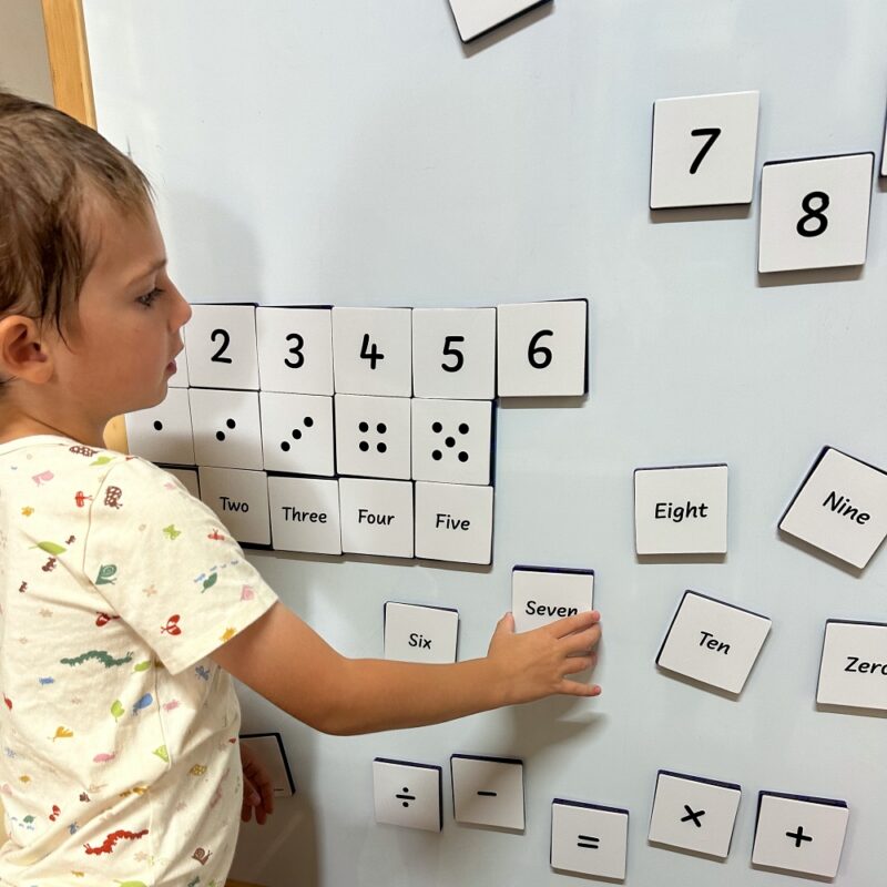 Child using numeracy toppers on magnetic tiles on whiteboard