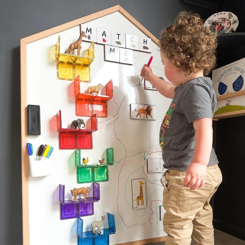 Child playing with tiles on a Learn & Grow Toys Multi-Board on a wall in a playroom