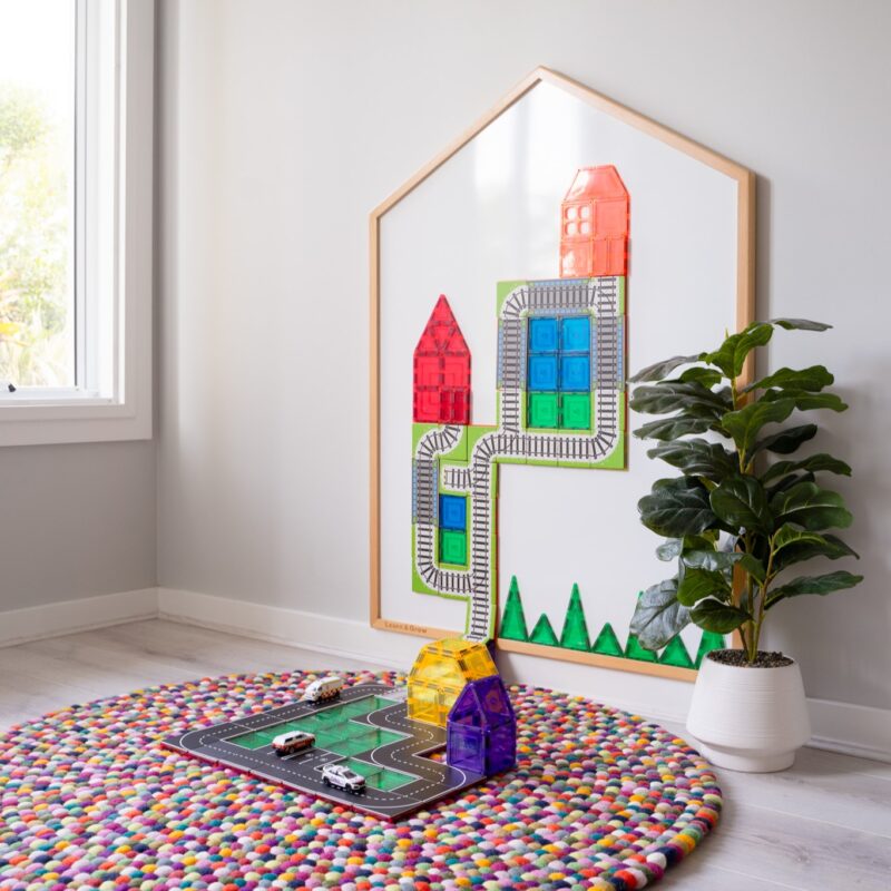 Learn & Grow Toys Multi-Board on wall in playroom with road and train toppers on board and multi-coloured rug on floor
